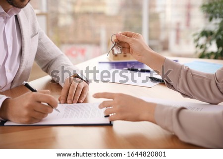 Real estate agent giving key with trinket to client in office, closeup