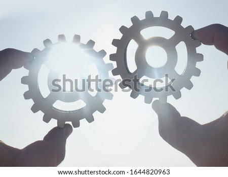 two hands businessman holding gears on the background of blue sky in the sun, connecting the puzzle pieces. creation. mechanism. Business idea concept, teamwork, strategy, innovation, cooperation