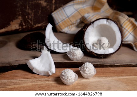 Coconut and sweet chocolate truffles. Coconut shell, flakes, small pieces of crashed nut and white chocolate sweets on a wooden background. Tropical fruit coconut in the shell. 
