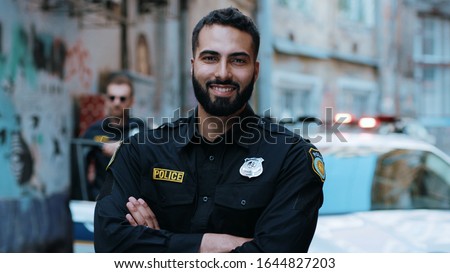 Smiling young man cops stand near patrol car look at camera enforcement happy officer police uniform auto safety security communication control policeman portrait close up slow motion Royalty-Free Stock Photo #1644827203