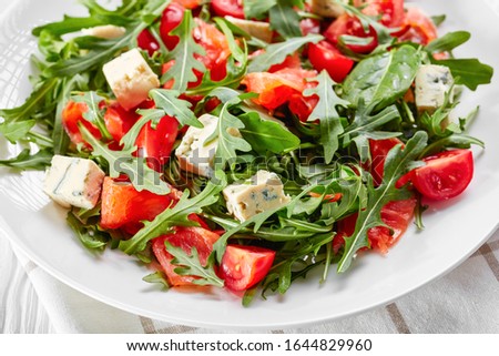 close-up of delicious healthy salmon arugula blue cheese tomato salad on a white plate on a wooden table, horizontal view from above, macro