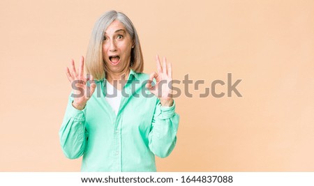 middle age cool woman feeling shocked, amazed and surprised, showing approval making okay sign with both hands