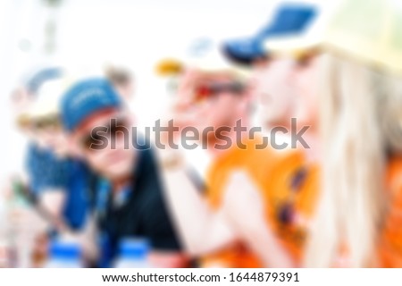 
a group of young people have fun and drink together at a race festival (Orange dutch racing fans, supporters), brurred picture, people drinking alcohol in the summer