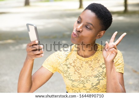 Mature lady showing peace sign and blowing kiss for selfie. Cheerful mature lady holding phone in arm and posing for self portrait. Self portrait, gesture concept