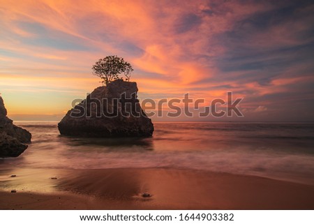 Amazing seascape. Beach during sunset. Rock with tree in the ocean. Waves captured with slow shutter speed. Long exposure with soft focus. Pink and orange sky with clouds. Bingin beach, Bali Indonesia