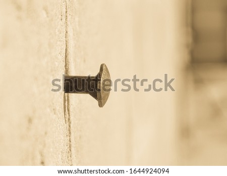 
A hat of a thick rusty nail or bolt sticking out of a gray concrete wall. Old vintage retro photo.