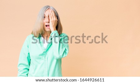 middle age cool woman looking sleepy, bored and yawning, with a headache and one hand covering half the face