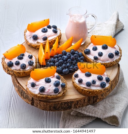 Sweet buns with soft cheese, blueberry and slice of persimmon on white wooden table