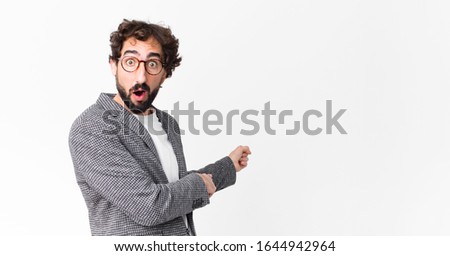 young crazy businessman feeling shocked and surprised, pointing to copy space on the side with amazed, open-mouthed look against flat wall