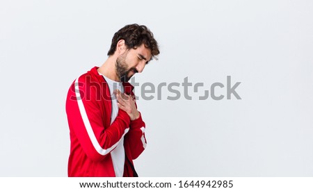 young bearded man back view looking sad, hurt and heartbroken, holding both hands close to heart, crying and feeling depressed against copy space wall