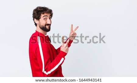 young bearded man back view smiling and looking happy, friendly and satisfied, gesturing victory or peace with both hands against copy space wall