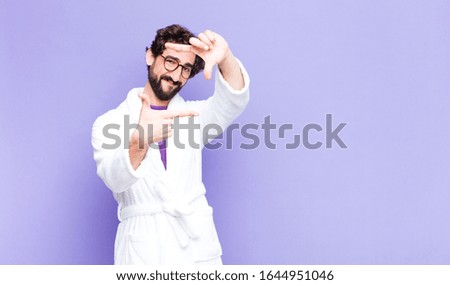 young bearded man wearing bathrobe feeling happy, friendly and positive, smiling and making a portrait or photo frame with hands