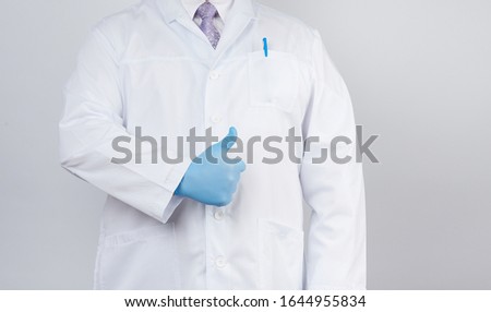 doctor in a white coat and tie shows with his hand a gesture like, wearing blue latex medical gloves, white background, copy space
