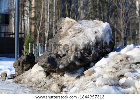 Plenty of snow piled with a lot of small rocks photographed during a sunny spring day in Finland. You can also see some trees of a small forest in the background. Color image, synny spring day.