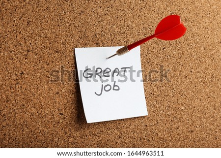  sheet of paper with text "great job" attached with a dart to a cork board