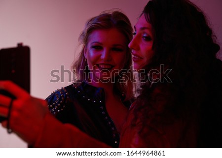 Two young women take selfie in studio, red photo