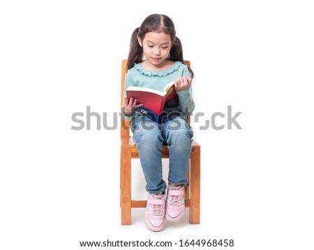 Asian little cute girl 6 years old sitting on wood chair and reading the book. Preschool lovely kid with the book. Learning and education of kid. Royalty-Free Stock Photo #1644968458