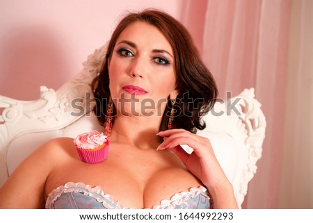 A cupcake on the shoulders of a beautiful young woman in a dress with bare shoulders and a deep neckline. Sits on a white chair with different back.