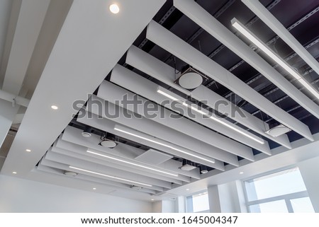linear LED lights and sound absorbing ponies hang on a plasterboard ceiling with integrated spotlights Royalty-Free Stock Photo #1645004347