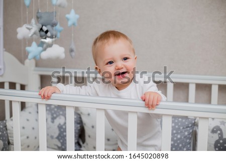 healthy baby smiling in white cnjbn clothes in a baby bed, holding on to the side of the bed, space for text