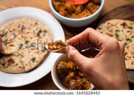 Close-up of image of woman having food, Potato curry (Kashmiri dum aloo) with chapatti (roti) on wooden dining table.  Royalty-Free Stock Photo #1645028443