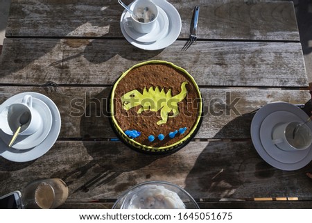 A top view shot of a yellow t-rex chocolate birthday cake on a wooden table
