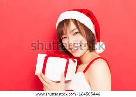 young woman with Santa hat holding Christmas gift against red background