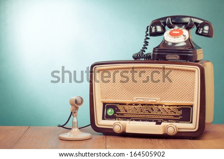 Retro radio with green light, microphone and telephone on wooden table