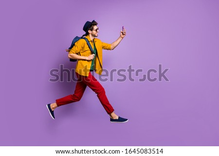 Full size profile side photo of cheerful guy in retro headwear holding blue bag jump run make selfie on smartphone wear yellow shirt red pants trousers isolated over violet color background Royalty-Free Stock Photo #1645083514