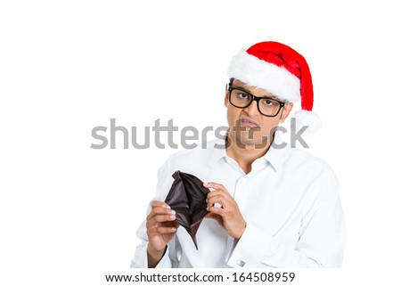 Closeup portrait of young man in red santa claus hat with big black glasses holding up showing empty wallet, isolated on white background with space to left. Negative human emotion facial expression