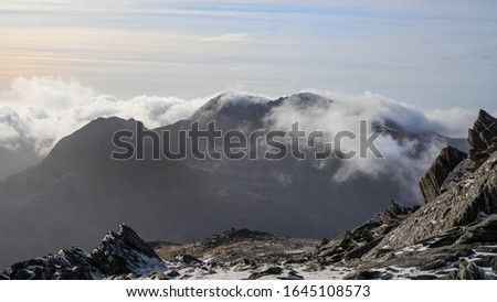 Wide aerial view of a snowcapped Mount Snowdon with low cloud and blue skies in Wales