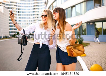 Fashion couple of beautiful trendy elegant woman wearing summer color matching classic feminine outfits, bags and sunglasses, making selfie end enjoying time together, traveling mood, summertime.