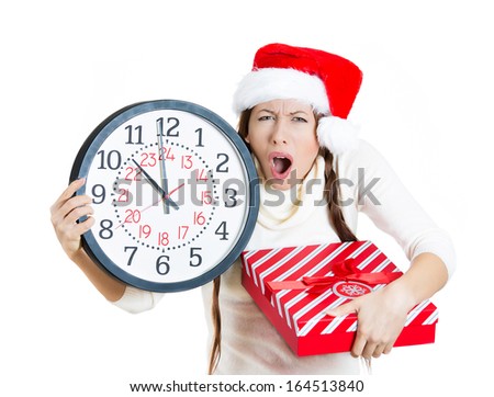 Closeup portrait of worried, stressed young woman wearing red santa claus hat, holding clock and a gift box, isolated on white background. Emotion, facial expression. Last minute christmas shopping