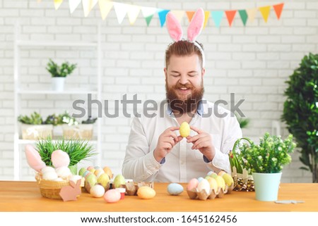 Happy easter.A funny fat man decorates eggs while sitting at a table with easter decor in the background