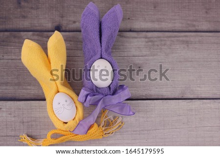 Happy easter concept.Easter holiday table setting with eggs on barn boards. Rabbits from eggs, yellow and purple napkins with bows on wooden background. Top view with copy space for text.