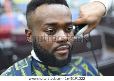 Black man in the Spanish barbershop. Cute black man makes a haircut in the African salon. Hair style. Haircut  for adults.  Royalty-Free Stock Photo #1645191322