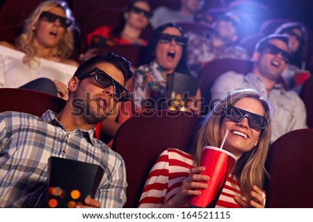 Young people sitting at cinema, watching 3D film, smiling.