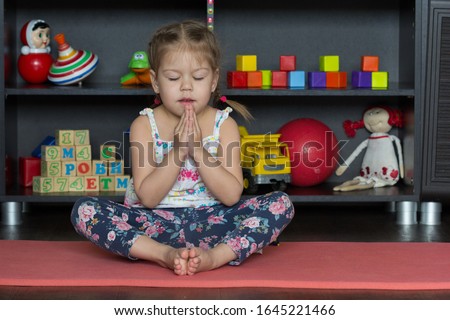Little girl making yoga pose of cobbler or butterfly as sit on buttocks with tall spine, bend legs, place soles of feet together, and gently flap legs like wings of butterfly with close eyes