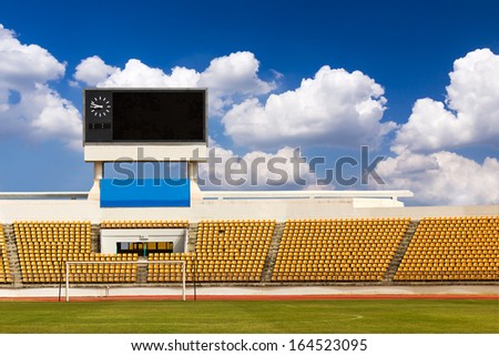 Rows of orange seats on the stadium with scoreboard displaying clock above them