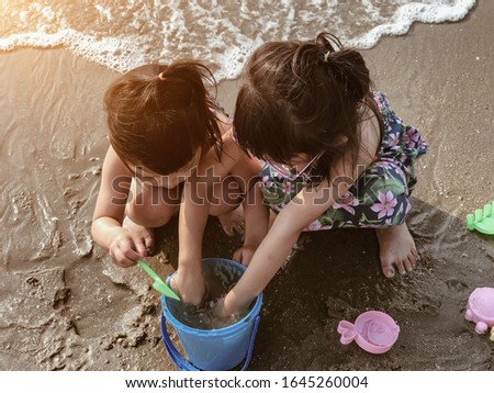 Two little girl plays in the sand on the beach on a summer holiday.