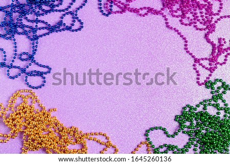 Carnival shiny beads, traditional carnaval accessories. Mardi gras frame or border on purple background, masquerade masks and beads flat lay, copy space, top view