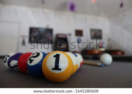 Billard balls on a pool table in the garage. There is a bar in the background  with pictures and decorations. 