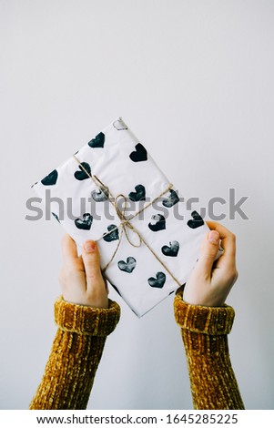 a cute gift in a woman's hand wrapped in homemade wrapping paper with black hearts tied with jute thread for Valentine's day on a white background