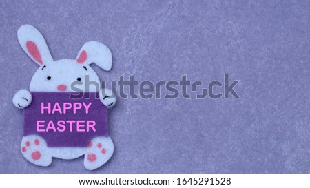 felt craft easter bunny holding a blank sign on a purple background with writing space