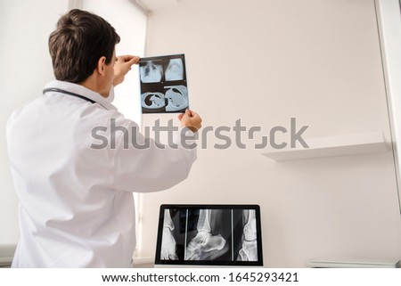 Back view of young man radiologist doctor holding and analysis x ray and computed tomography film