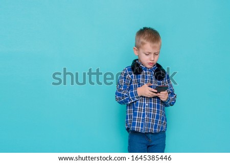 Funny little boy playing video game on cellphone, children entertainment on blue background
