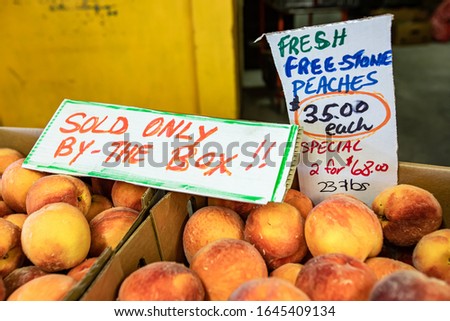 Close up neatly arranged cardboard boxes of bright orange peaches with hand written price sign. Fresh fruit at the local market. Selective focus.
