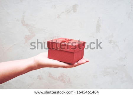 Hand holding a red gift box on a gray background, congratulation, holiday