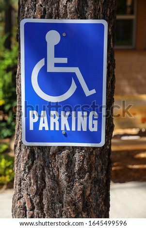 A handicap parking sign on a tree trunk .