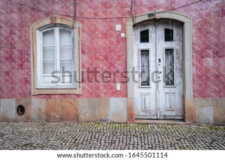 Lovely white door surrounded by pink tiles in Silves, Portugal, with cobblestone street